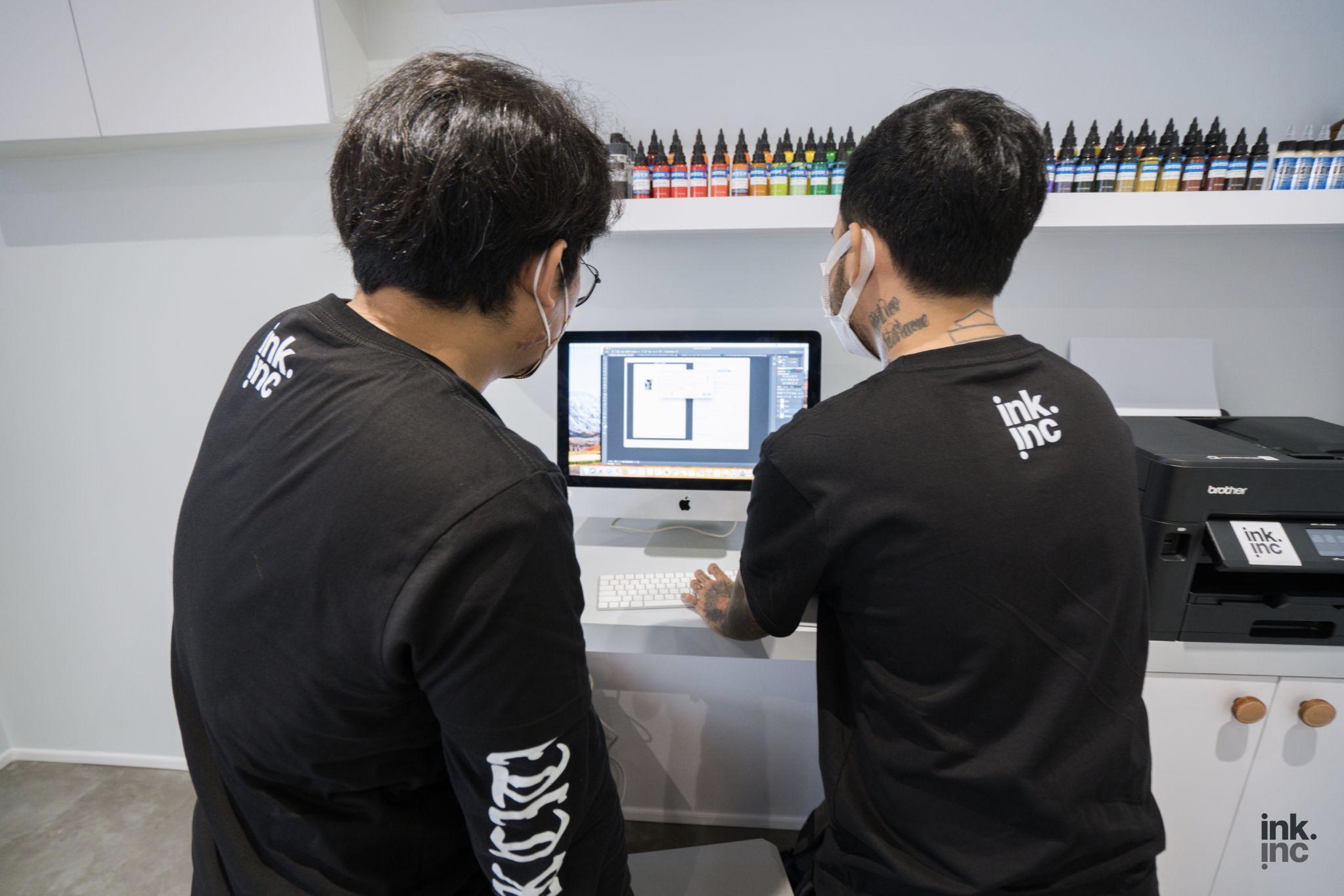 two tattoo artists in front of a computer
